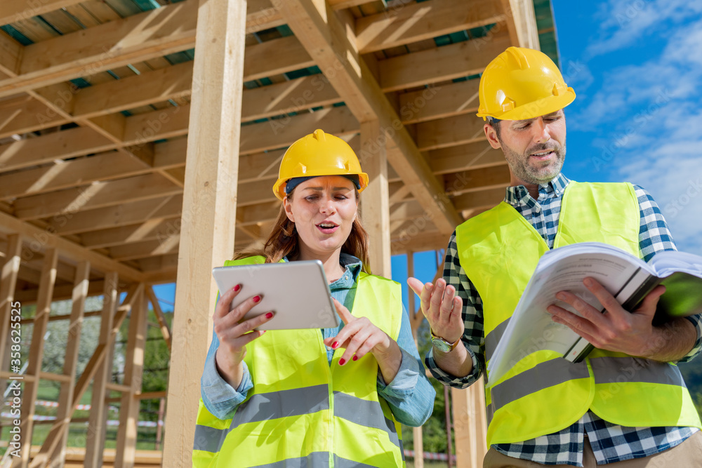 Construction engineer and architect consult plans on building site of wood framing house under const