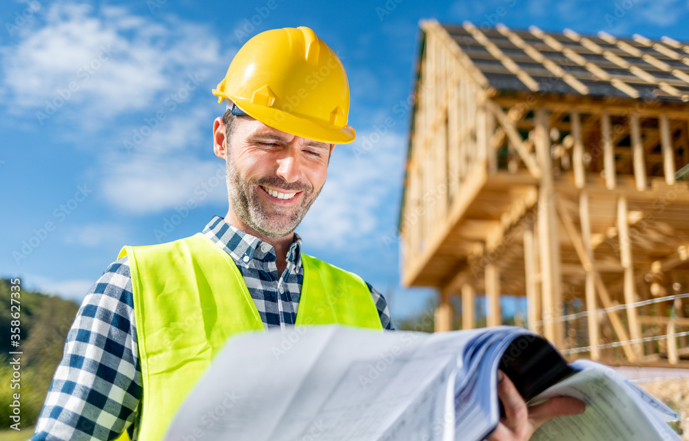 Architect on building site looking at blue prints house plans