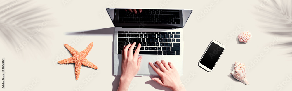 Person using a laptop computer with shells and starfish - flat lay