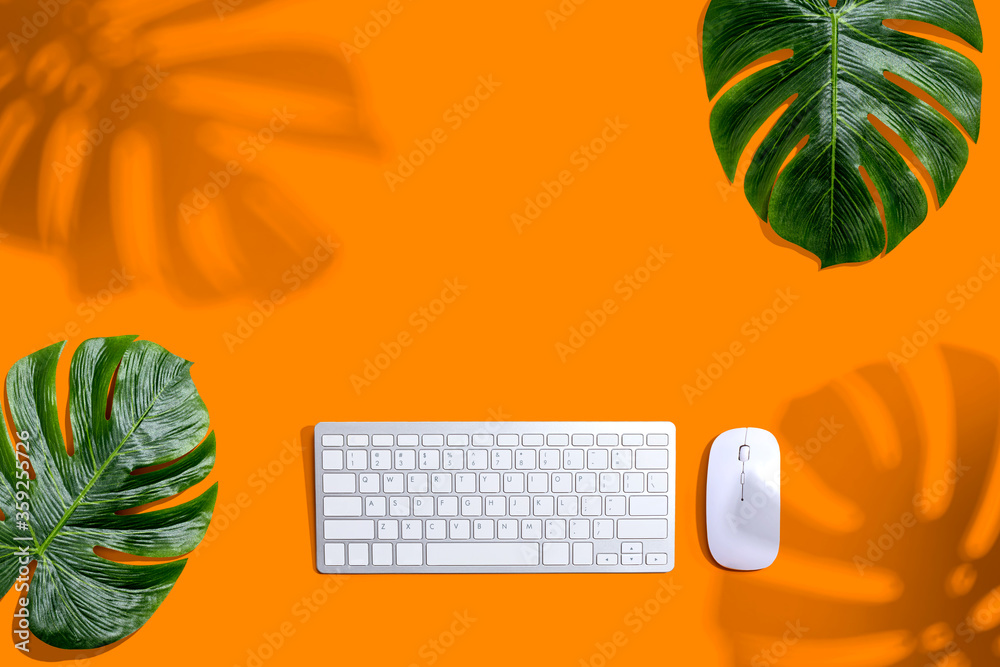 Computer keyboard with tropical leaves and shadow - flat lay