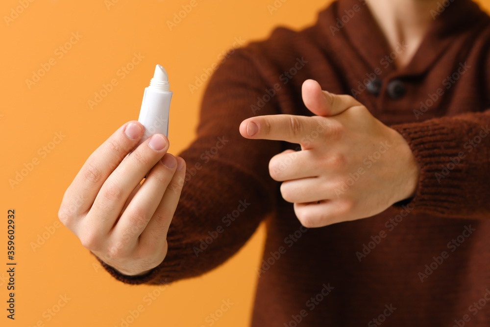 Handsome young man with lip balm on color background, closeup