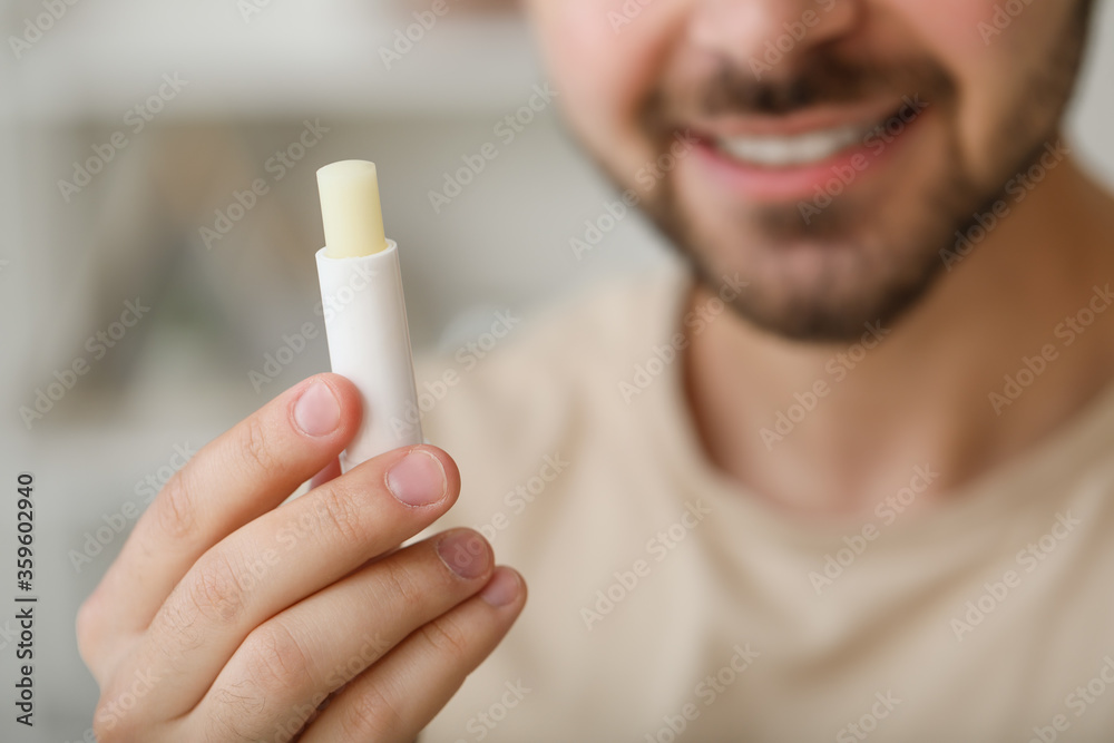 Handsome young man with lip balm at home, closeup