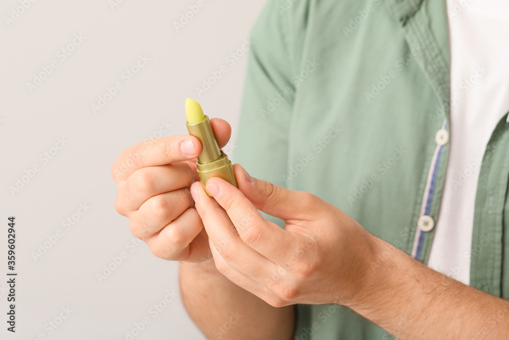 Handsome young man with lip balm on light background, closeup