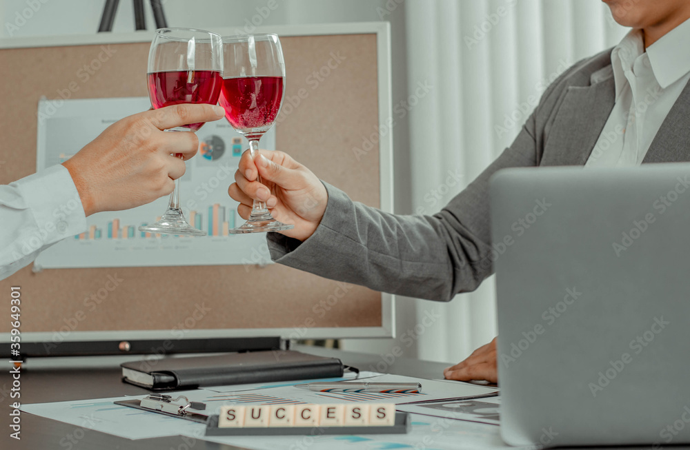 Two businessmen are sipping wine in the office, working to celebrate the success of the company busi