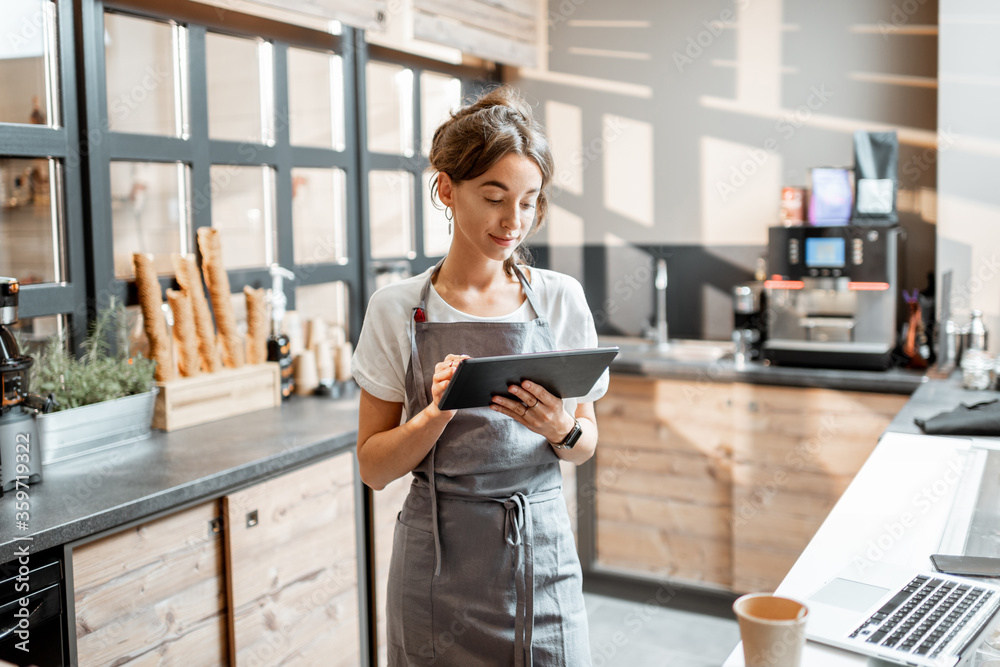 Young saleswoman working with a digital tablet at the counter of cafe or confectionary shop. Concept