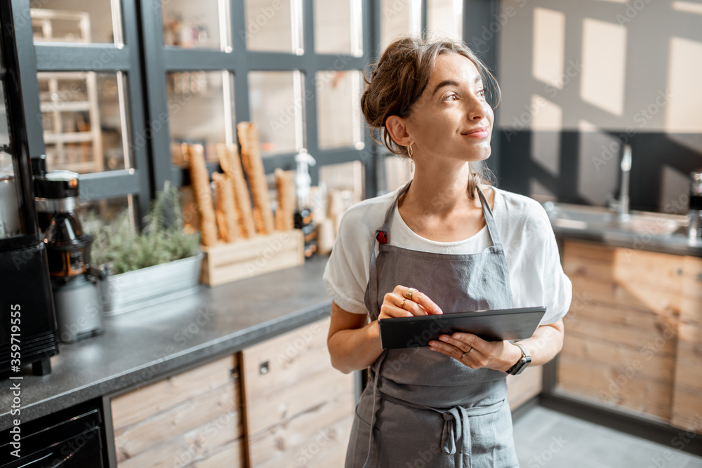 Young saleswoman working with a digital tablet at the counter of cafe or confectionary shop. Concept