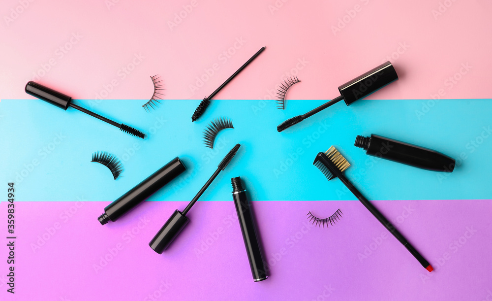 Black mascara and fake eyelashes with brush on color background