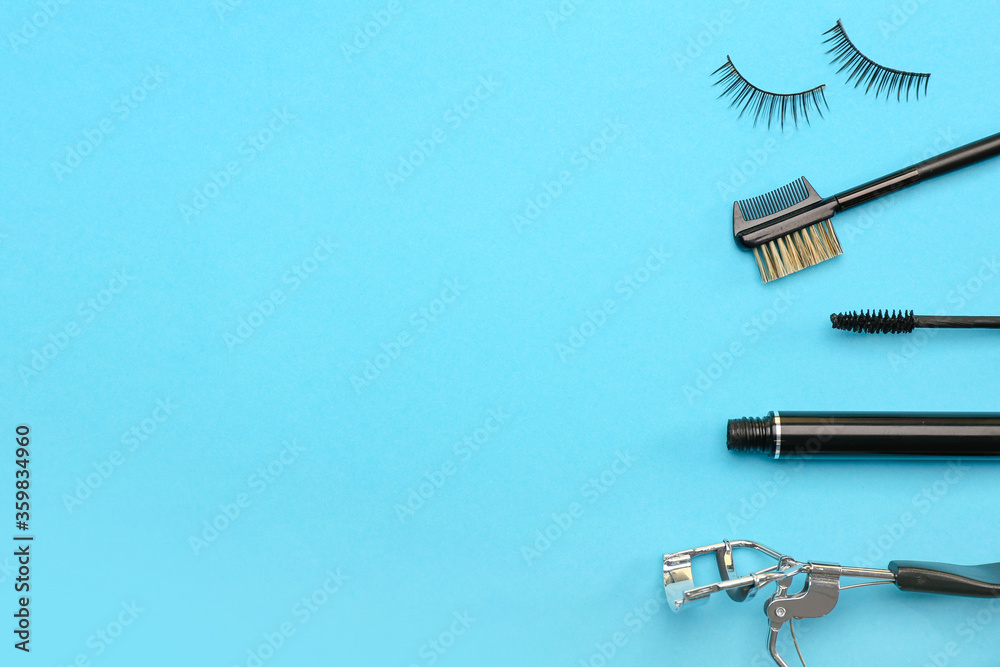 Black mascara, fake eyelashes, brush and curler on color background