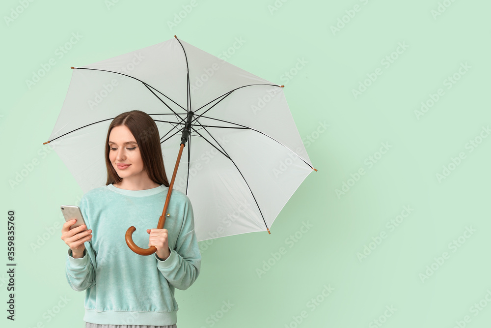 Beautiful woman with umbrella and mobile phone on color background