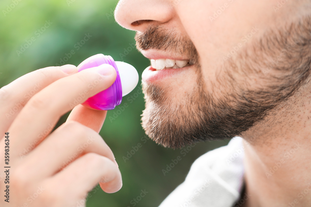 Handsome young man with lip balm outdoors, closeup