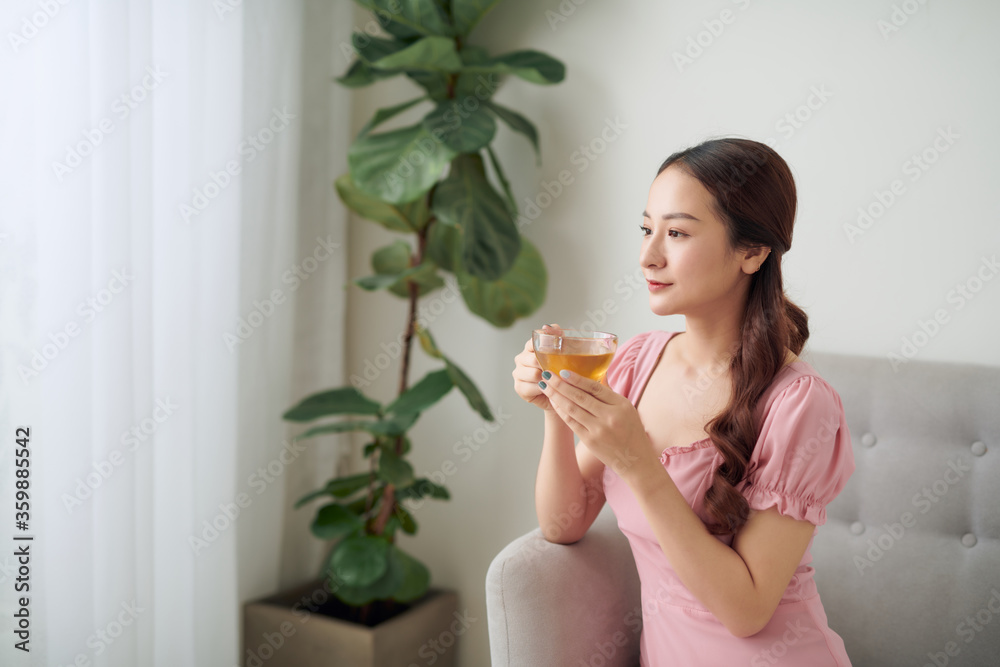 迷人的年轻女子在家里的沙发上放松时喝着一杯咖啡