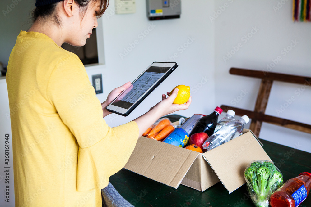 宅配で届いた食品の情報をタブレットで確認する女性