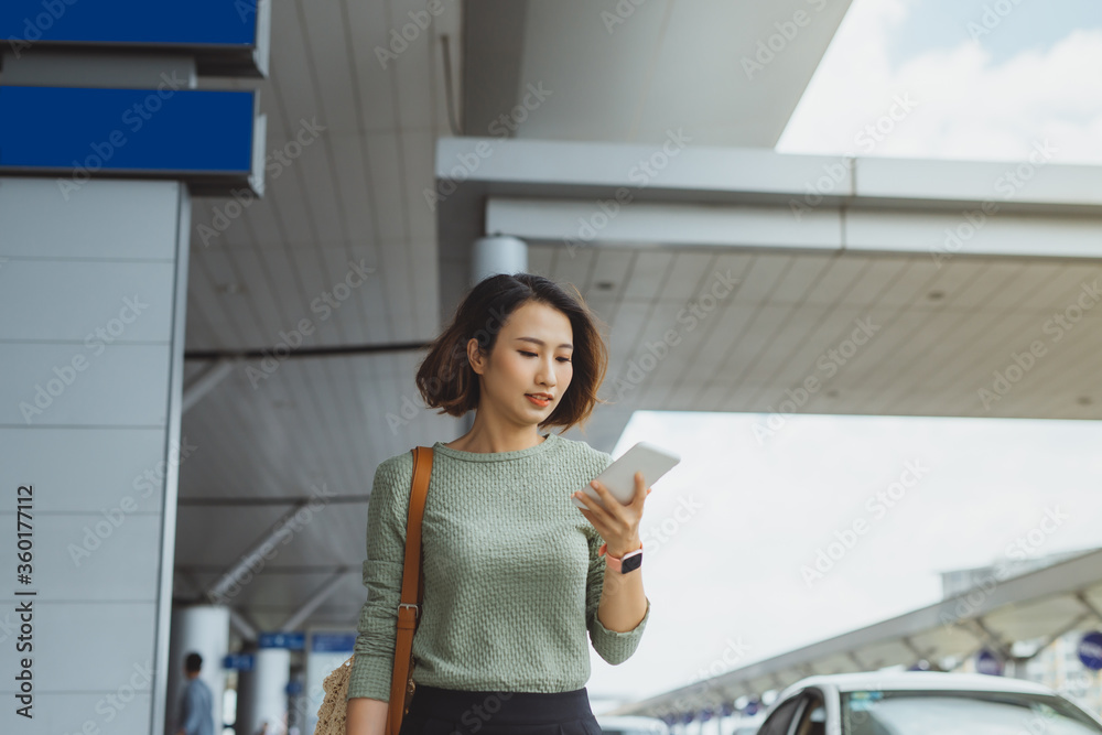 年轻的女商人站在外面用电话检查航班。