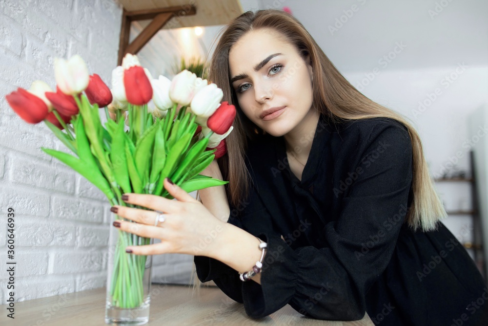 Close-up cute girl looking to the viewer, holding a bouquet of tulips in a vase with her hands. Home