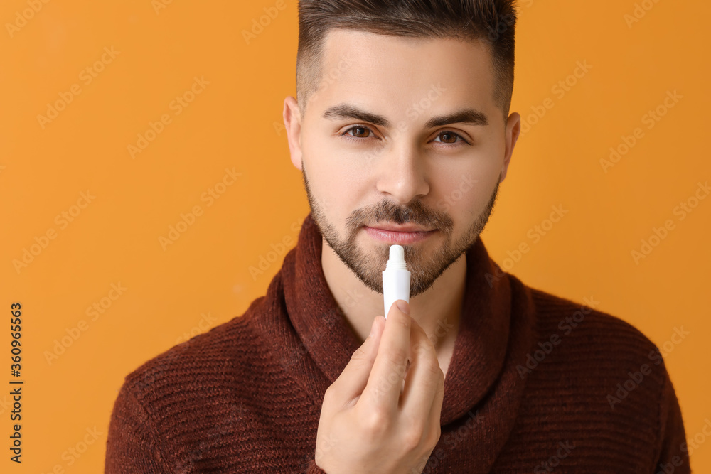 Handsome young man with lip balm on color background