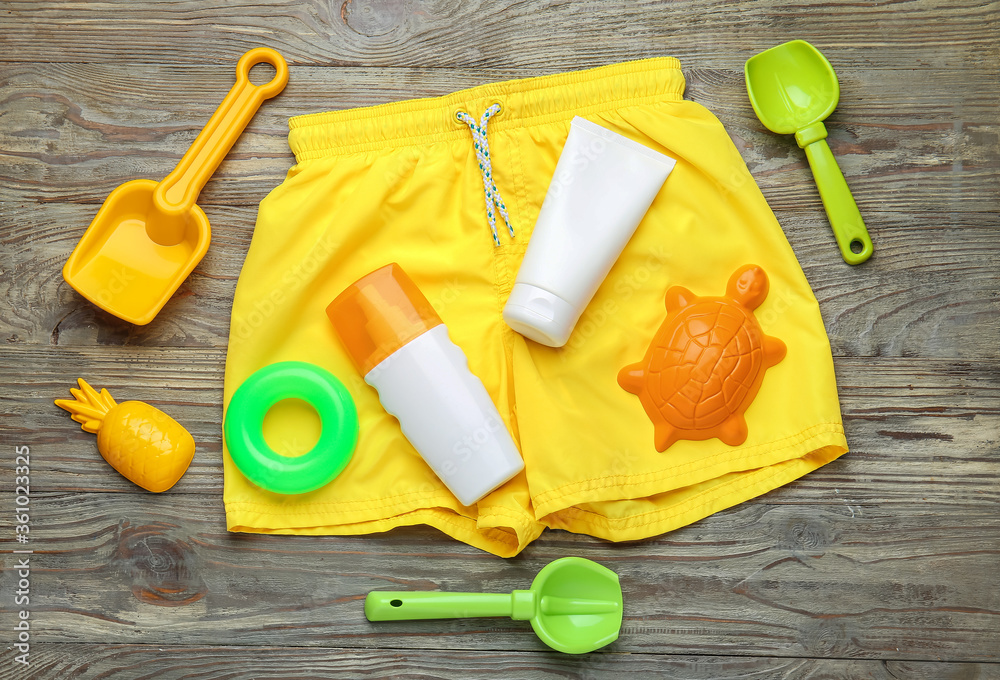 Sunscreen cream with beach sand toys and swimsuit on wooden background