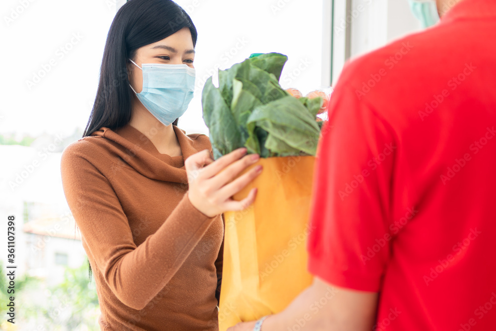 一位戴着口罩的亚洲女士，从一家超市买了新鲜食品、蔬菜和水果