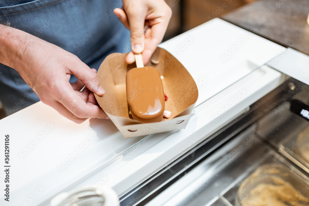 Seller making chocolate ice cream with toppings at the shop, close-up