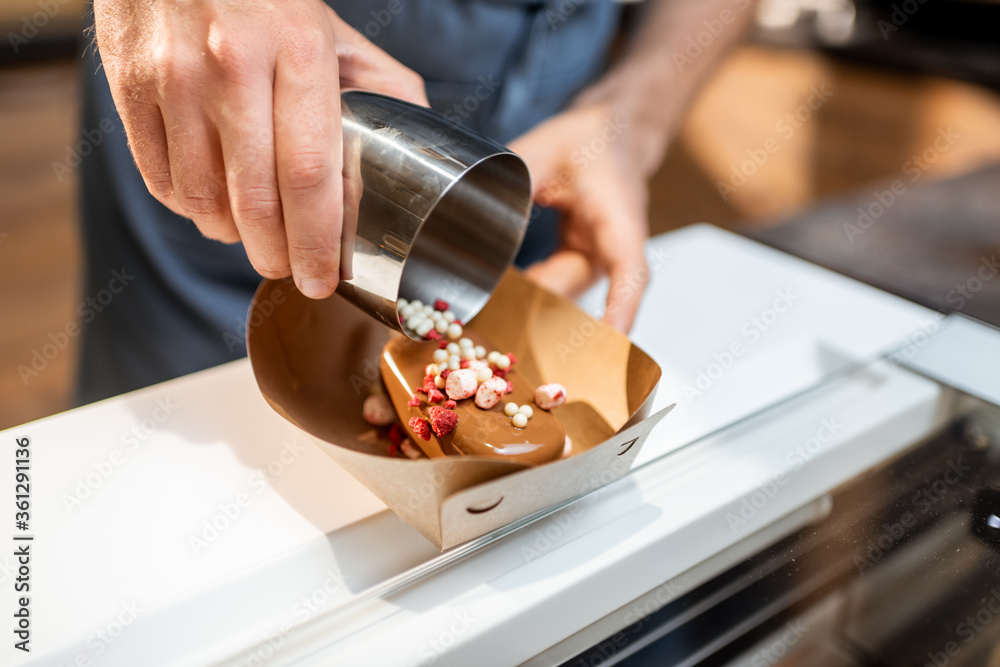 Seller making chocolate ice cream with toppings at the shop, close-up