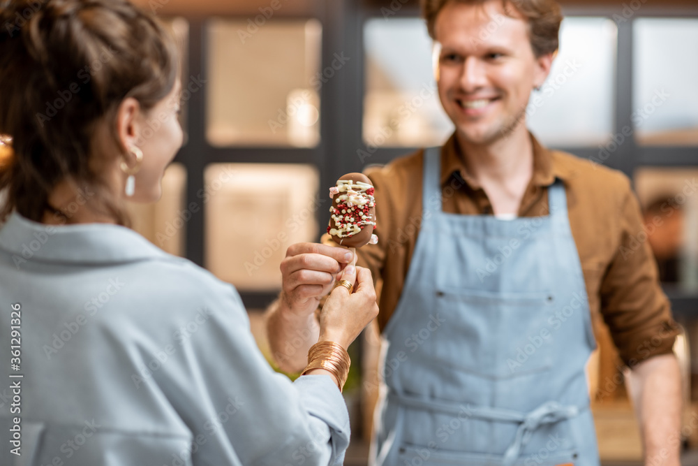 Portrait of a cheerful salesman in uniform selling ice cream for a young woman client at the shop