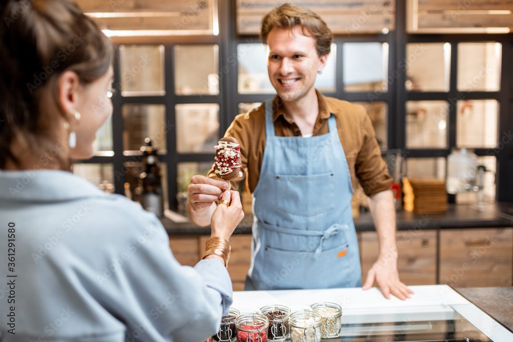 Portrait of a cheerful salesman in uniform selling ice cream for a young woman client at the shop