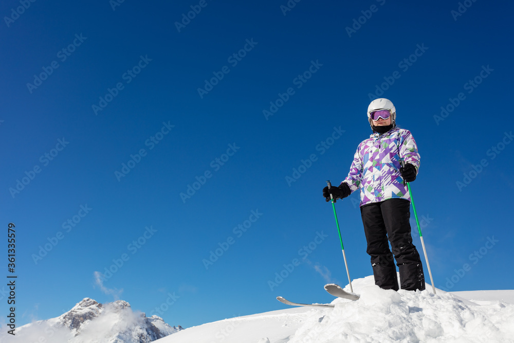 自信酷炫的滑雪女孩穿着运动装备站在蓝天上的雪堆上