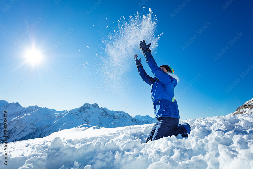 Profile view of teen girl throw snow in the air over blue sky and high mountain tops on background