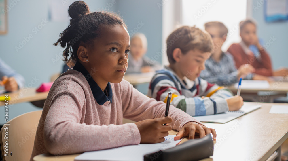 In Elementary School Classroom Brilliant Black Girl Writes in Exercise Notebook, Taking Test and Wri