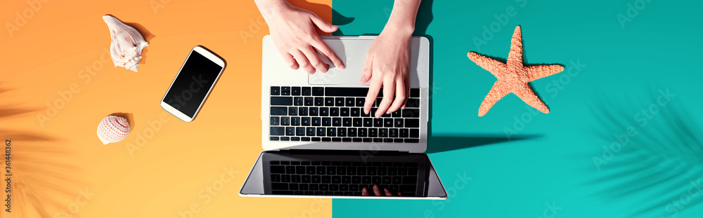 Person using a laptop computer with shells and starfish - flat lay