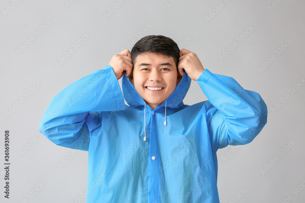 Young Asian man in raincoat on grey background