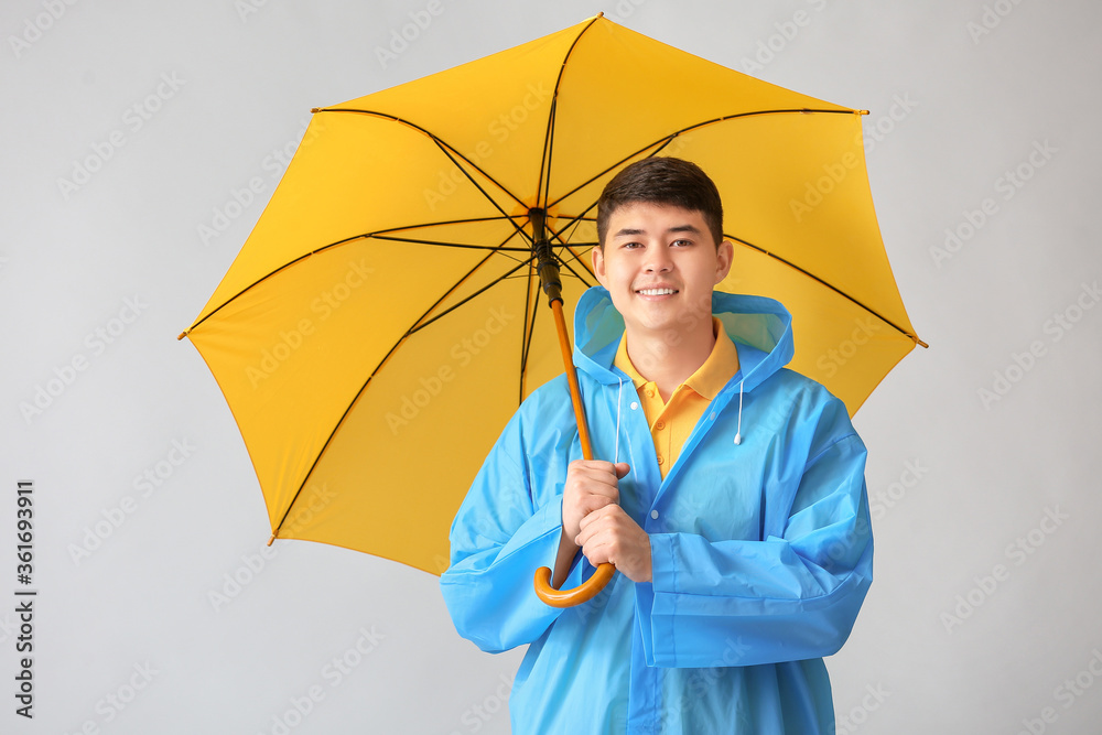 身穿雨衣、灰色背景带伞的亚洲年轻男子