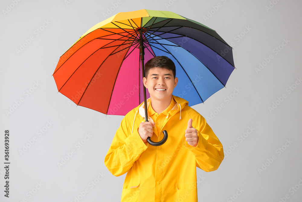 身穿雨衣、灰色背景带伞的亚洲年轻男子