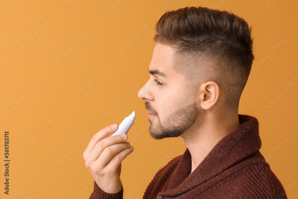 Handsome young man with lip balm on color background