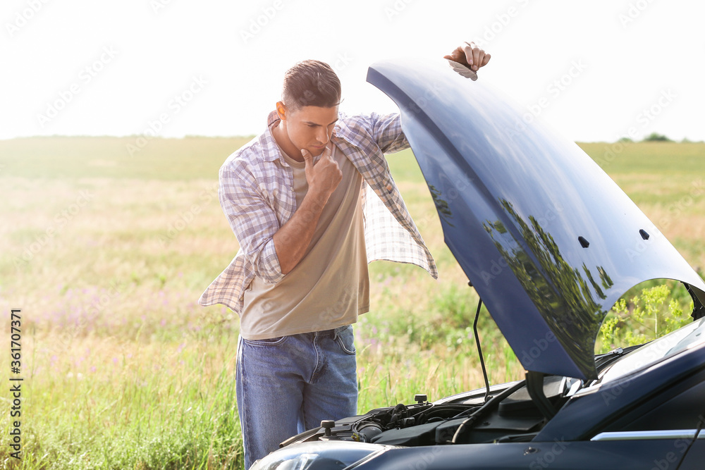 Young man near broken car on road