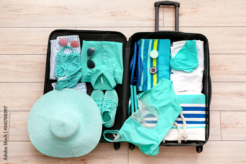 Packed suitcase with beach accessories on wooden background. Travel concept