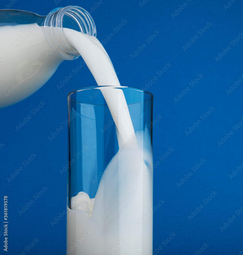 Pouring milk in glass isolated on blue background