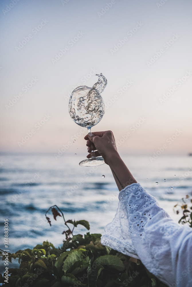 女人们穿着白色蕾丝连衣裙袖子，手里拿着一杯白色流动的葡萄酒，葡萄酒里有水滴和美丽的阳光