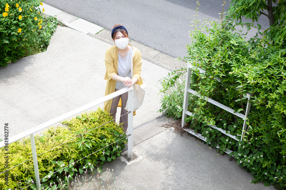 社会的距離をとって玄関から部屋の中の友人に声をかけるマスクの女性