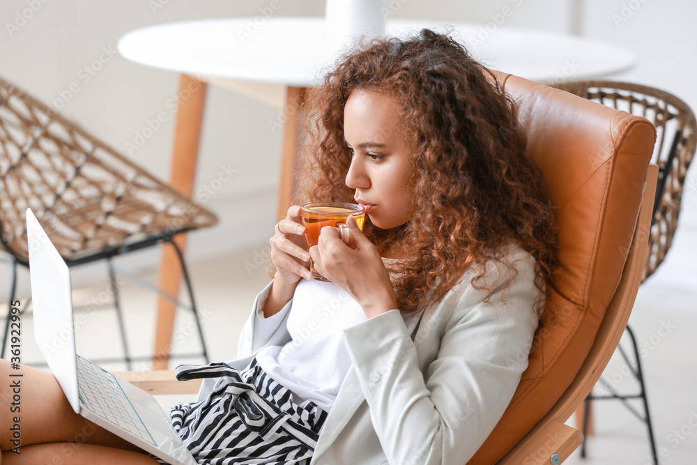 Beautiful young African-American woman with laptop drinking hot tea at home