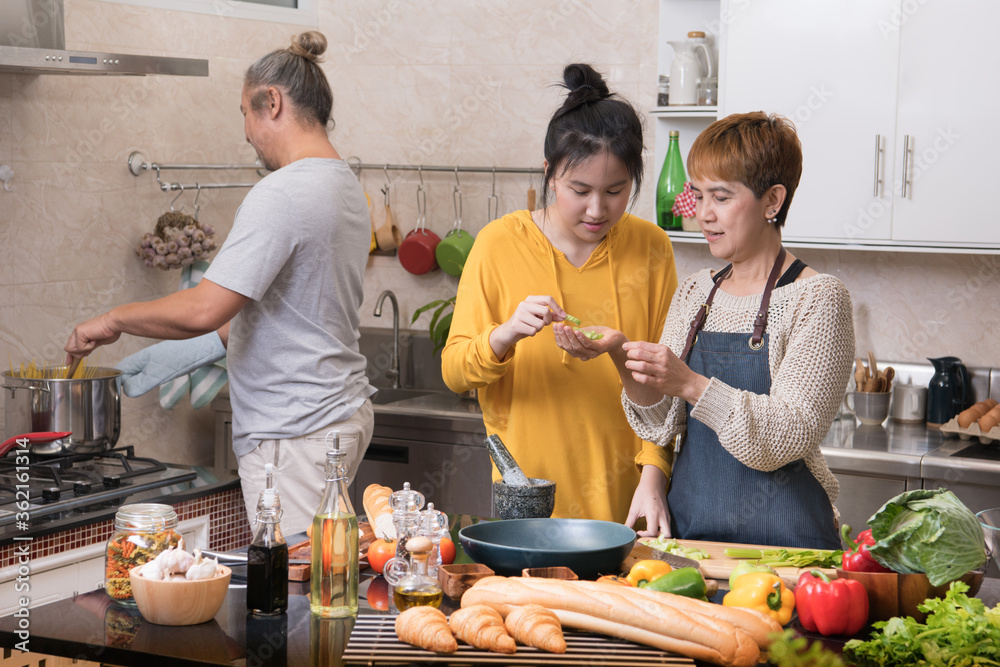 快乐的亚洲家庭，母亲、父亲和女儿在厨房烹饪，一起制作健康食品