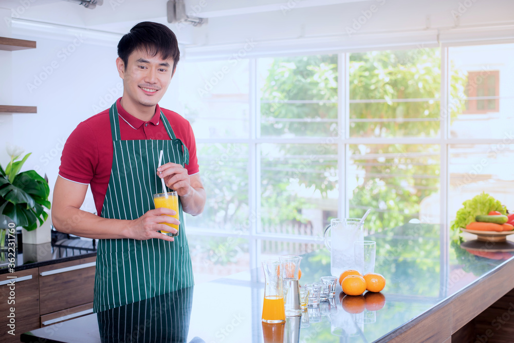 一名年轻的亚洲男子正在做橙汁奶昔。在家隔离时，在现代化的厨房里