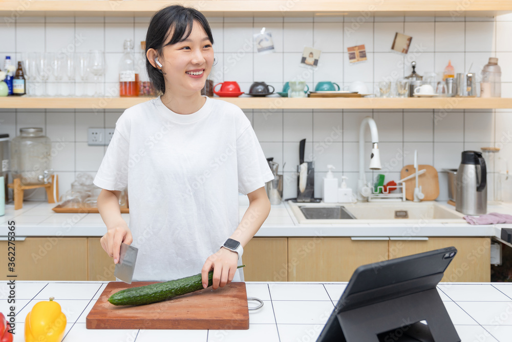 一个清纯的女孩一边切菜一边玩平板电脑