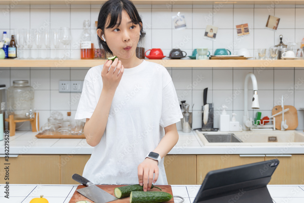 一个清纯的女孩一边切菜一边玩平板电脑