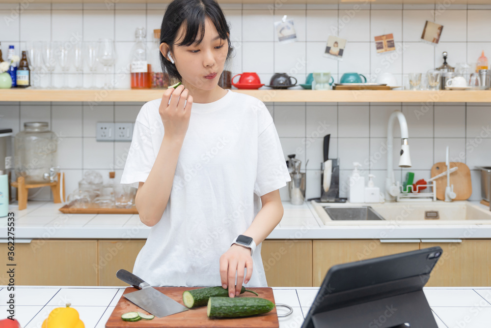 一个清纯的女孩一边切菜一边玩平板电脑