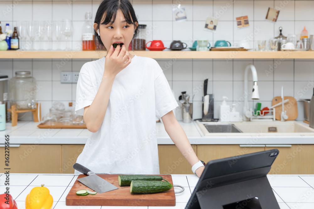 一个清纯的女孩一边切菜一边玩平板电脑