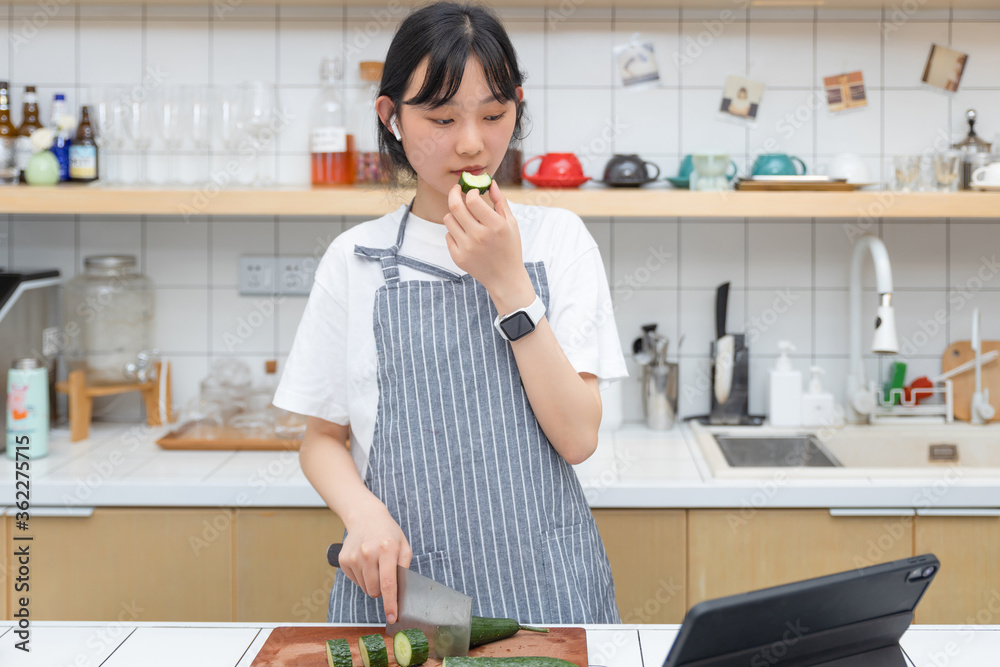 一个清纯的女孩一边切菜一边玩平板电脑