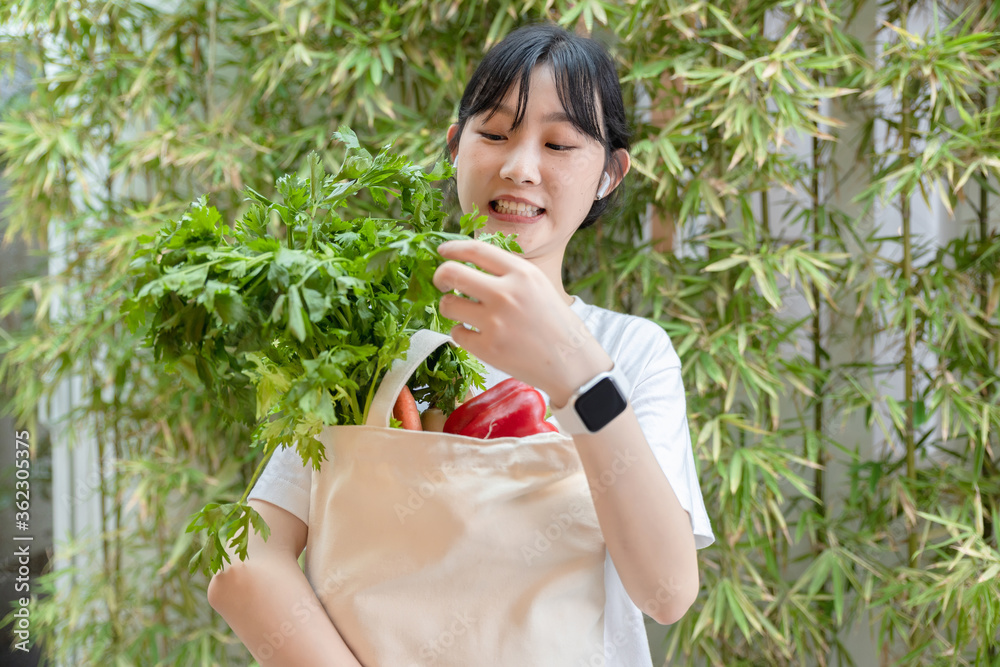 美丽纯洁的亚洲女孩，用帆布包裹蔬菜，手里拿着水杯