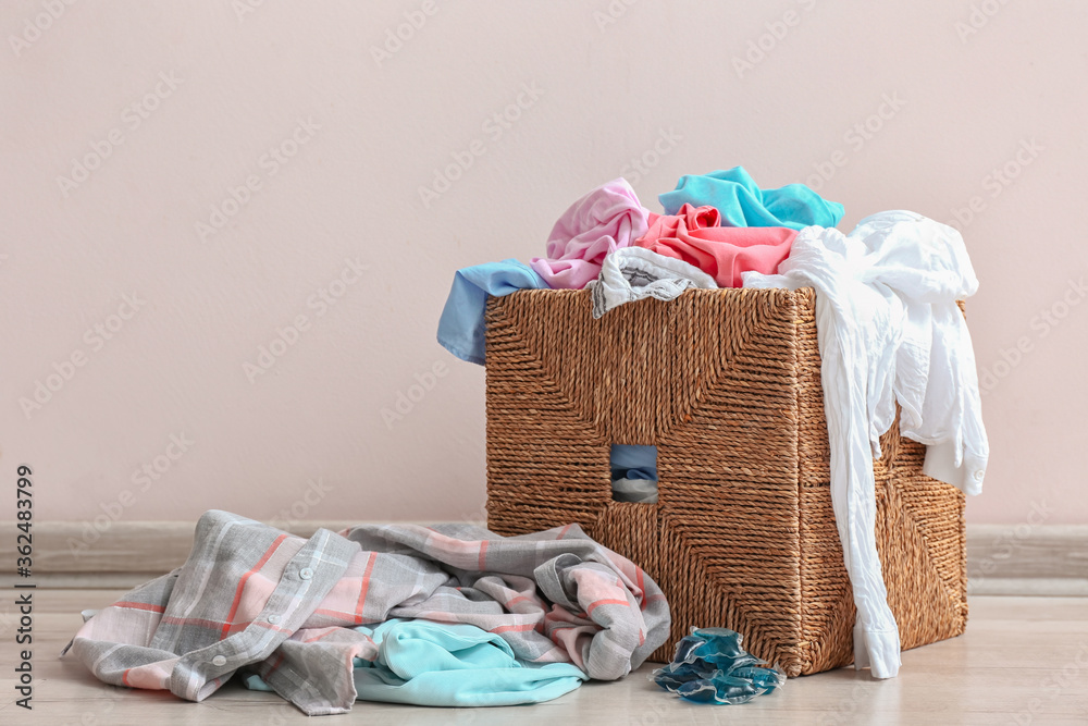 Basket with dirty clothes near light wall