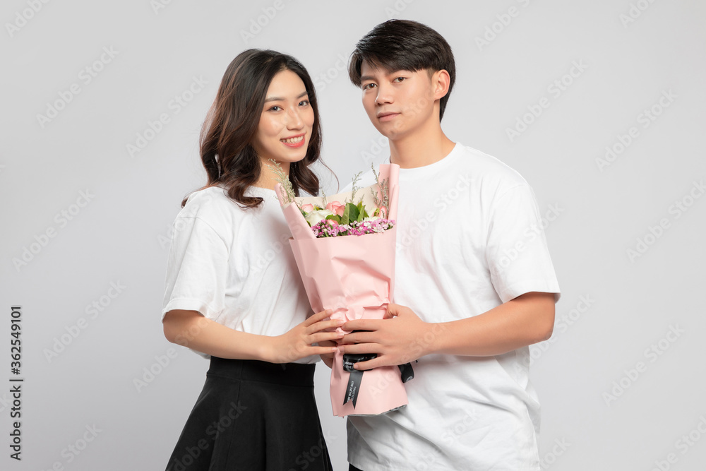 Young Asian lovers with flowers in their hands against a gray background

