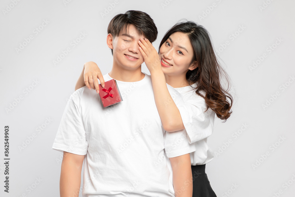 Young Asian lovers with gift boxes in their hands against a gray background

